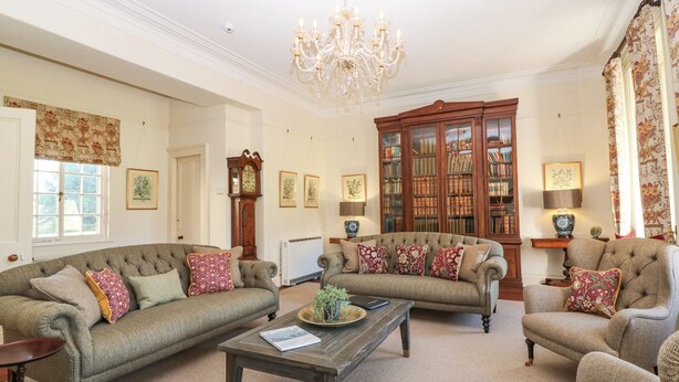 A traditional living room with two sofas, a coffee table, a chandelier, and a bookcase filled with books.