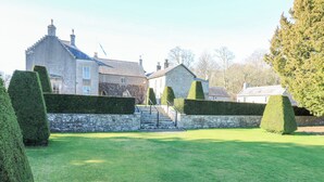 A well-maintained garden with neatly trimmed hedges and a stone wall leading to a building with multiple windows and a stone facade.