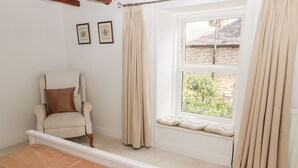 Ein Schlafzimmer mit Bett, Stuhl, einem Fenster mit Vorhängen und Blick auf Grünflächen.