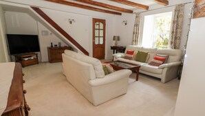 Ein Wohnzimmer mit einer Couch, einem Couchtisch und einem Fernseher. Eine Treppe führt in einen anderen Raum.