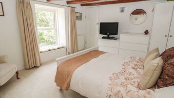 A bedroom with a bed, a television, a wardrobe, and a window with curtains.