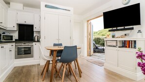 A modern kitchen with white cabinets, a dining table with chairs, a built-in oven, and a microwave. - 2 Garden Apartment (Kingsbridge)