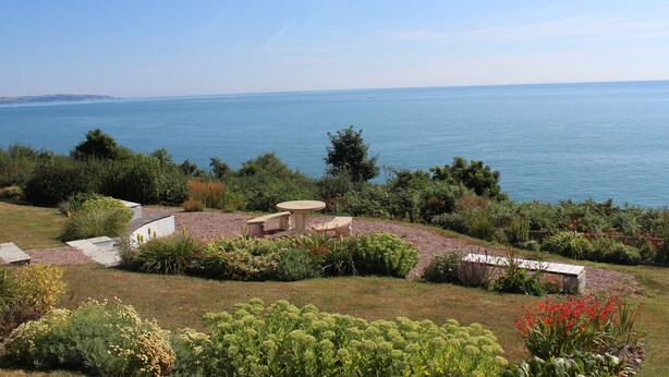 A coastal garden with a view of the sea, stone structures, and various plants. - 2 Garden Apartment (Kingsbridge)
