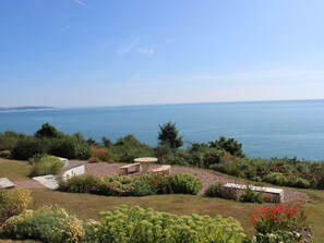 A coastal garden with a view of the sea, stone structures, and various plants. - 2 Garden Apartment (Kingsbridge)