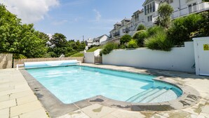 A rectangular swimming pool with a tiled deck, surrounded by a white wall and a wooden fence. - 2 Garden Apartment (Kingsbridge)