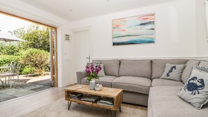 A modern living room with a grey sofa, a coffee table with books, and a painting on the wall. - 2 Garden Apartment (Kingsbridge)
