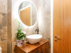 Un baño con tocador de madera, un lavabo blanco, un espejo y una planta en maceta.
