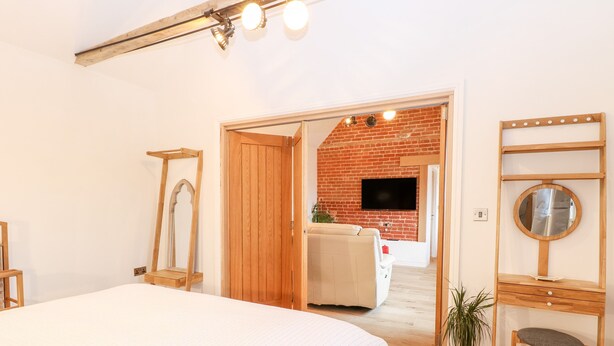 Ein Schlafzimmer mit einem großen Bett, einem Holzschrank, einem Spiegel und einem an einer Ziegelwand montierten Fernseher.