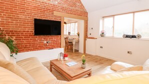 Ein Wohnzimmer mit Backsteinwand, einem Flachbildfernseher über einem Holztisch und einem Fenster mit Jalousien.