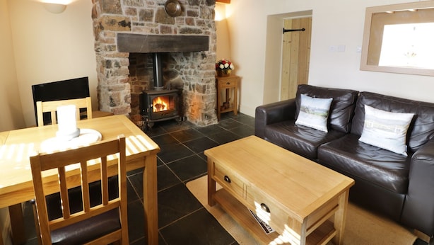 A cozy living room with a stone fireplace, wooden furniture, and a leather sofa. - Menai Cottage (Llanfairpwllgwyngyll)