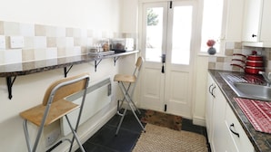 A compact kitchen with a countertop, two chairs, a door, and a sink. - Menai Cottage (Llanfairpwllgwyngyll)
