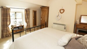 A bedroom with a large bed, a wooden wardrobe, a radiator, and heart-shaped decorations on the wall. - Menai Cottage (Llanfairpwllgwyngyll)