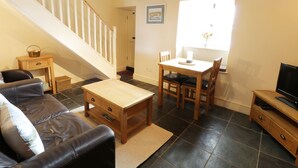 A cozy living room with a staircase, a dining area, and a TV stand. - Menai Cottage (Llanfairpwllgwyngyll)