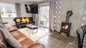 A modern living room with a leather sofa, a flat-screen TV, a fireplace, and a patterned wall. - Meadow View (Tyn-y-Gongl)