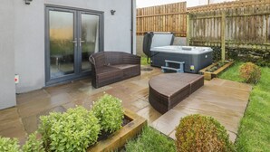 A patio with a hot tub, wicker furniture, and a wooden fence. - Meadow View (Tyn-y-Gongl)
