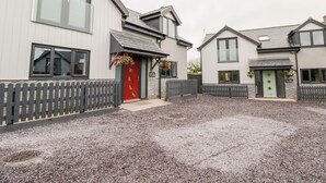 A modern residential building with a red door, grey picket fence, and flower baskets. - Meadow View (Tyn-y-Gongl)