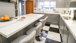 A modern kitchen with a central island, bar stools, and a black and white checkered floor. - Meadow View (Tyn-y-Gongl)