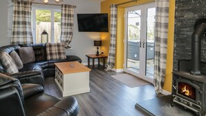Sala de estar com sofá de couro preto, mesa de centro de madeira, televisão de tela plana, lareira e porta de vidro deslizante que dá para uma área externa.