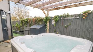 Un bain à remous installé à l’extérieur, sous une pergola en bois.