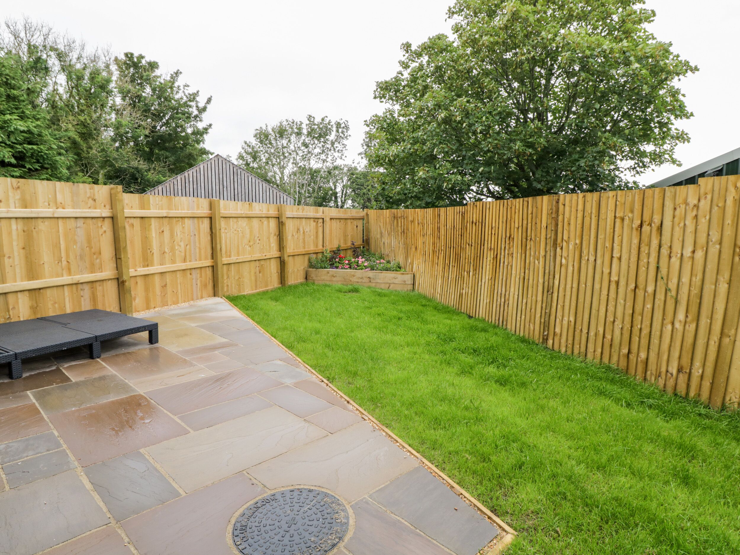A backyard with a wooden fence, a grassy area, and a paved patio with a bench.