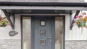 Une porte à double battant de couleur grise, avec un panneau de verre dépoli, une plaque de pierre portant l’inscription « Hunters Cottage », et deux jardinières de chaque côté.