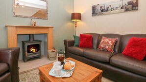 A cozy living room with a fireplace, leather sofa, and a coffee table with a tray of pastries. - 3 Old Hall Cottages (Bakewell)
