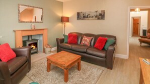A living room with a fireplace, leather sofa, wooden coffee table, and a painting on the wall. - 3 Old Hall Cottages (Bakewell)
