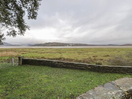 A rural landscape with a stone wall, grassy fields, and a distant hill.
