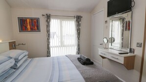 A hotel room with a bed, a TV, a mirror, and a window with curtains. - Oyster Bay Lodge (Dalbeattie)