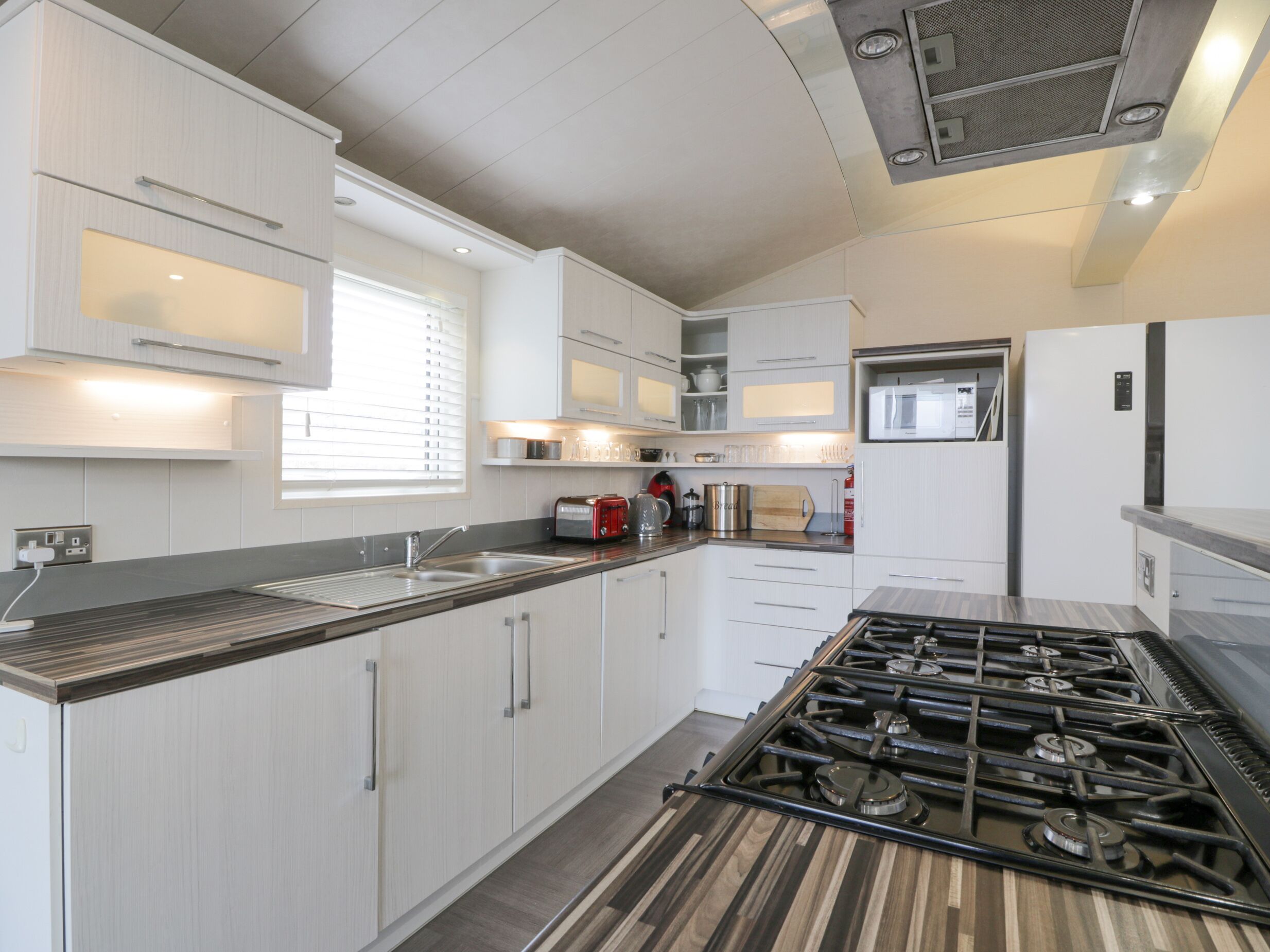Een moderne keuken met witte kastjes, een gasfornuis, een magnetron en een broodrooster.