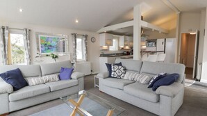 A modern living room with two grey sofas, a glass coffee table, and a view of a kitchen and dining area. - Oyster Bay Lodge (Dalbeattie)