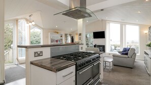 A modern kitchen with a built-in stove and oven, a glass chimney, and a large window overlooking a garden. - Oyster Bay Lodge (Dalbeattie)