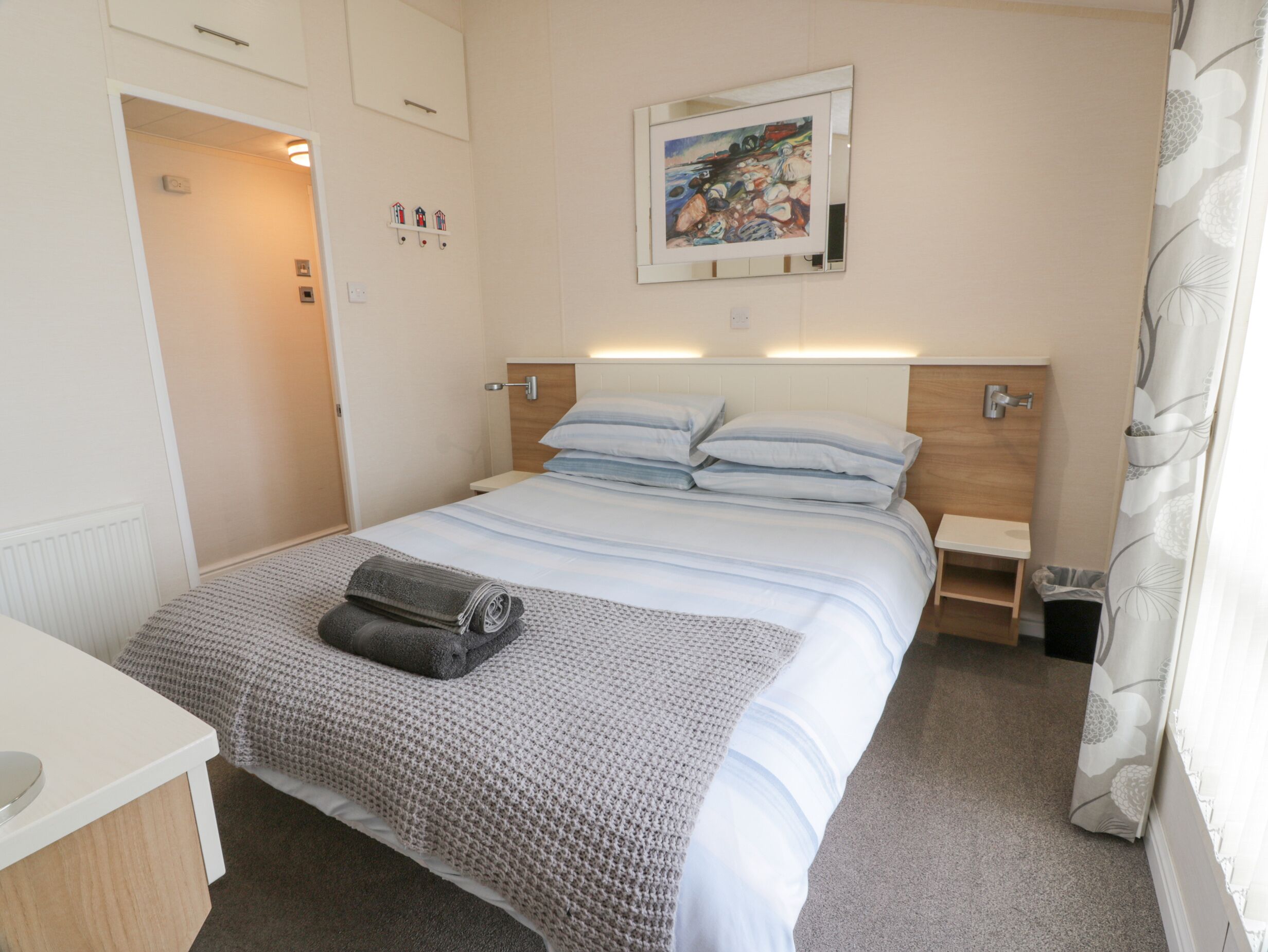 A neatly arranged bedroom with a bed, bedside tables, a painting, and a bathroom visible through an open door.