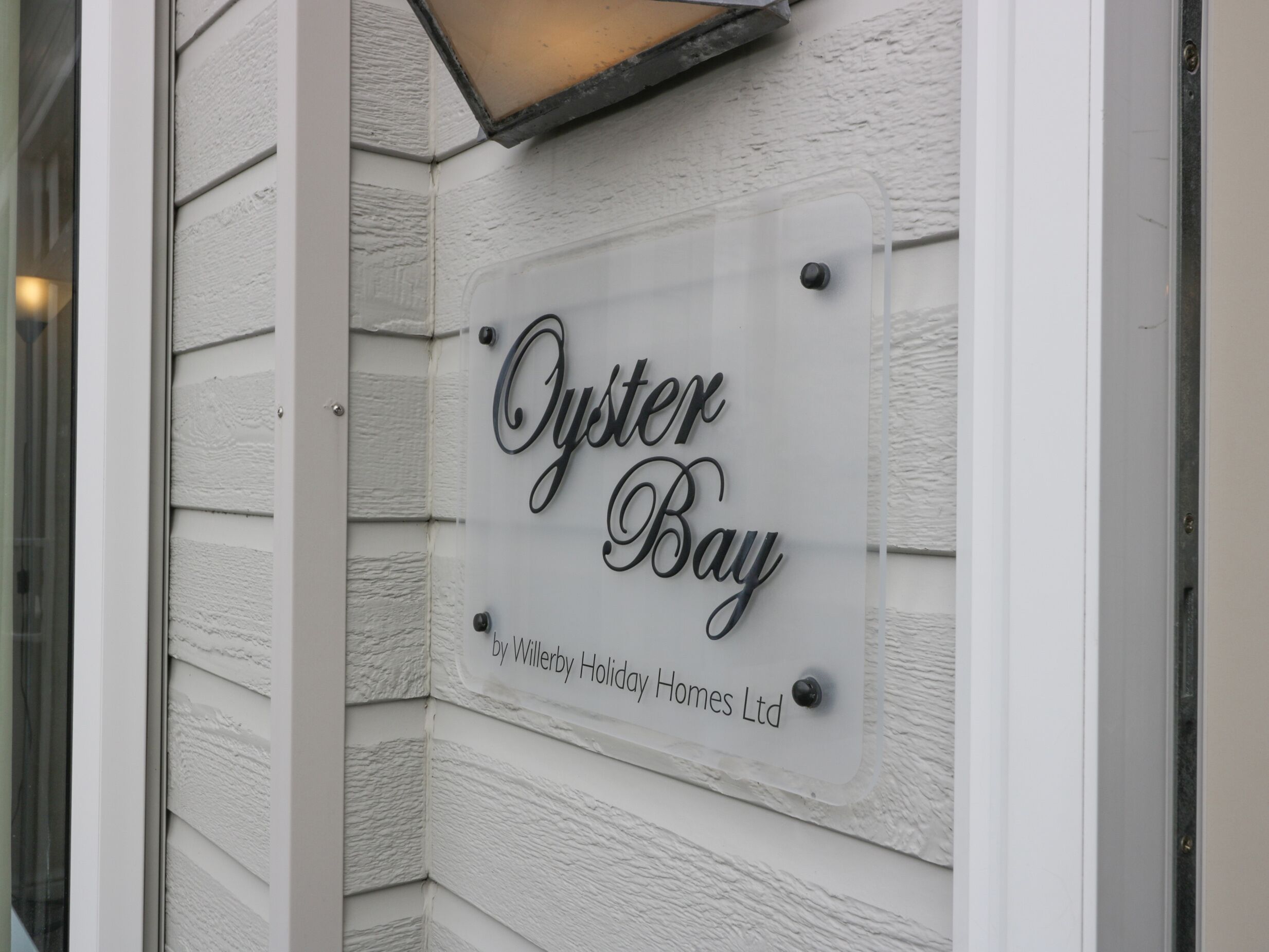 A sign reading "Oyster Bay by Willerby Holiday Homes Ltd" mounted on a white exterior wall.