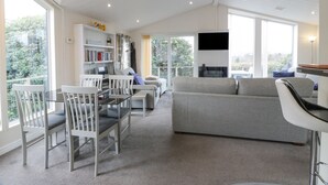A spacious living area with a grey sofa, white chairs, a glass table, and a bookshelf. - Oyster Bay Lodge (Dalbeattie)