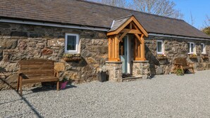 A stone building with a wooden porch, a bench, and potted plants. - Annex (Pwllheli)
