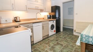A compact kitchen with white cabinets, a dishwasher, a washing machine, a microwave, and a refrigerator. - Annex (Pwllheli)
