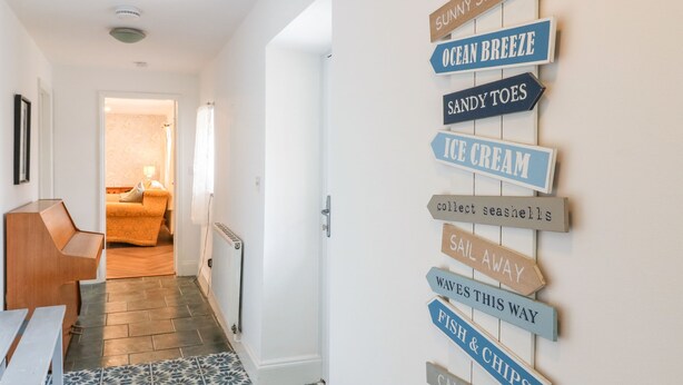 A hallway with a wall-mounted signpost listing amenities like 'Sunny Sea View', 'Ocean Breeze', and 'Ice Cream'. - Annex (Pwllheli)