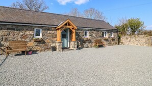 A stone building with a wooden door and windows, a gravel driveway, and a bench. - Annex (Pwllheli)