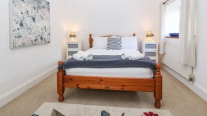 A neatly made bed with a polka dot blanket, two bedside lamps, a floral artwork on the wall, and a window with curtains. - Annex (Pwllheli)