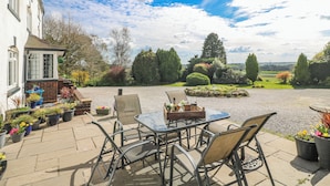 A patio with a table and chairs, surrounded by potted plants and a view of the countryside. - Fields Farm (Stoke-on-Trent)