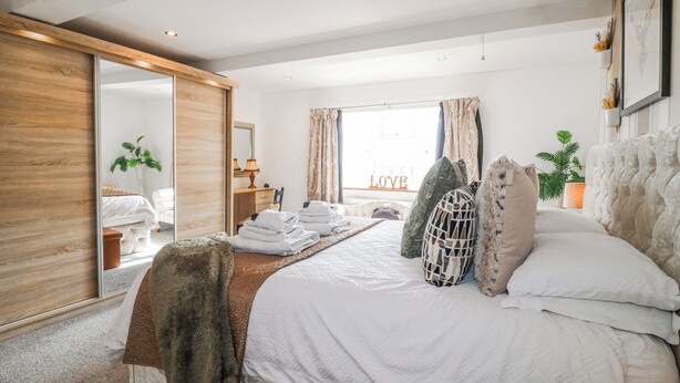 A bedroom with a bed, a mirror, a dresser, a window with curtains, and a view of the outside. - Fields Farm (Stoke-on-Trent)