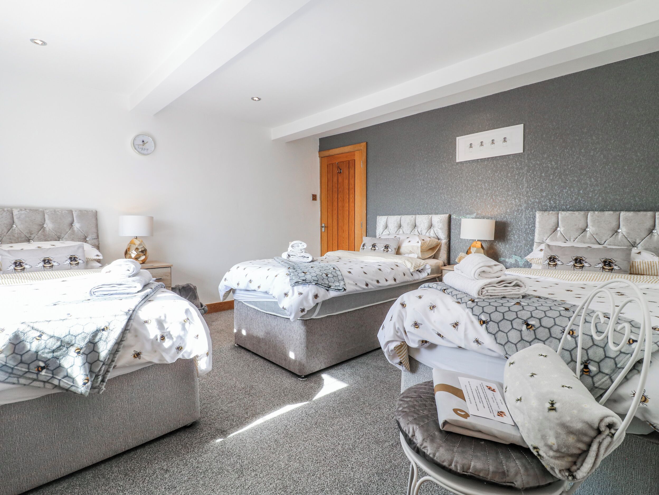 A hotel room with three beds, a wooden door, and a grey textured wall.