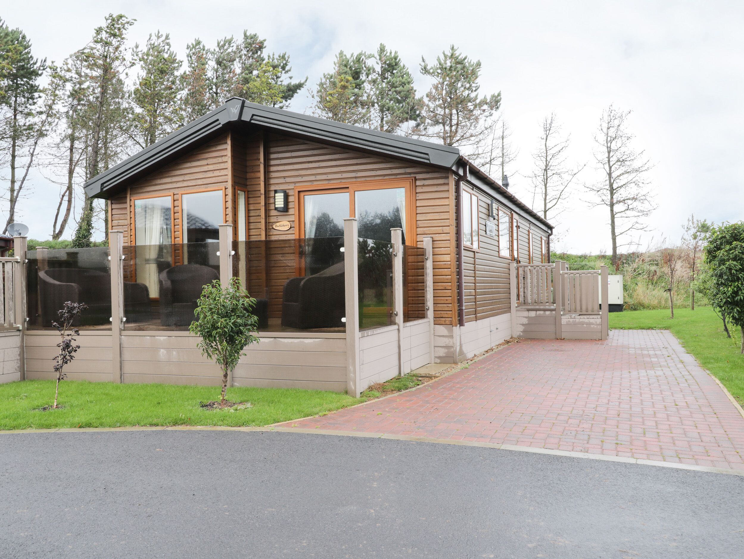 A wooden cabin with large windows, a covered porch, and a paved driveway.