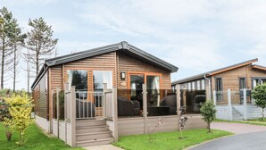 Eine Holzhütte mit Veranda, einem kleinen Garten und einer gepflasterten Auffahrt.