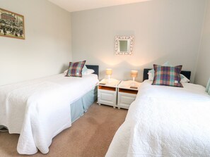 A twin room with two beds, each with a white duvet and a colorful pillow. There are bedside tables with lamps and a framed picture on the wall. - Beechwood Cottage (Pitlochry)