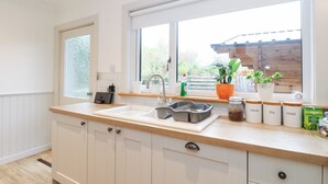Una cocina moderna con armarios blancos, un ventanal grande y una encimera con diversos objetos, incluyendo frascos etiquetados como café, té y azúcar.