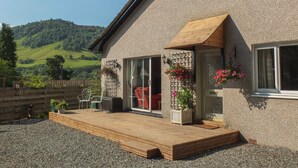 Una casa con terraza de madera, puerta de cristal y vista a una colina verde.