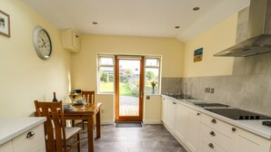 A kitchen with a dining area, featuring a stove, cabinets, and a window with a view of the outdoors. - Decca Cottage Nidd Grange (York)