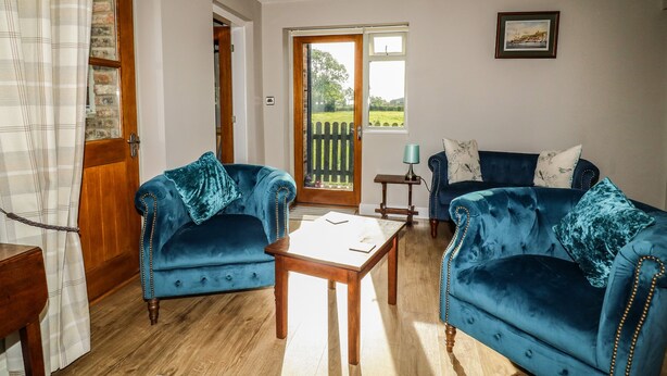 A living room with two blue velvet sofas, a wooden coffee table, and a wooden door leading to a balcony. - Decca Cottage Nidd Grange (York)